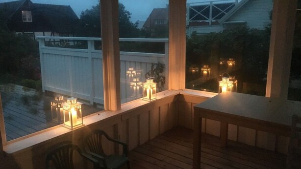 A covered outdoor area with a wooden deck, a table, and chairs. There are windows with lights on the inside. - "Torekov" mit Blick auf das Wasser by Interhome (Torekov)