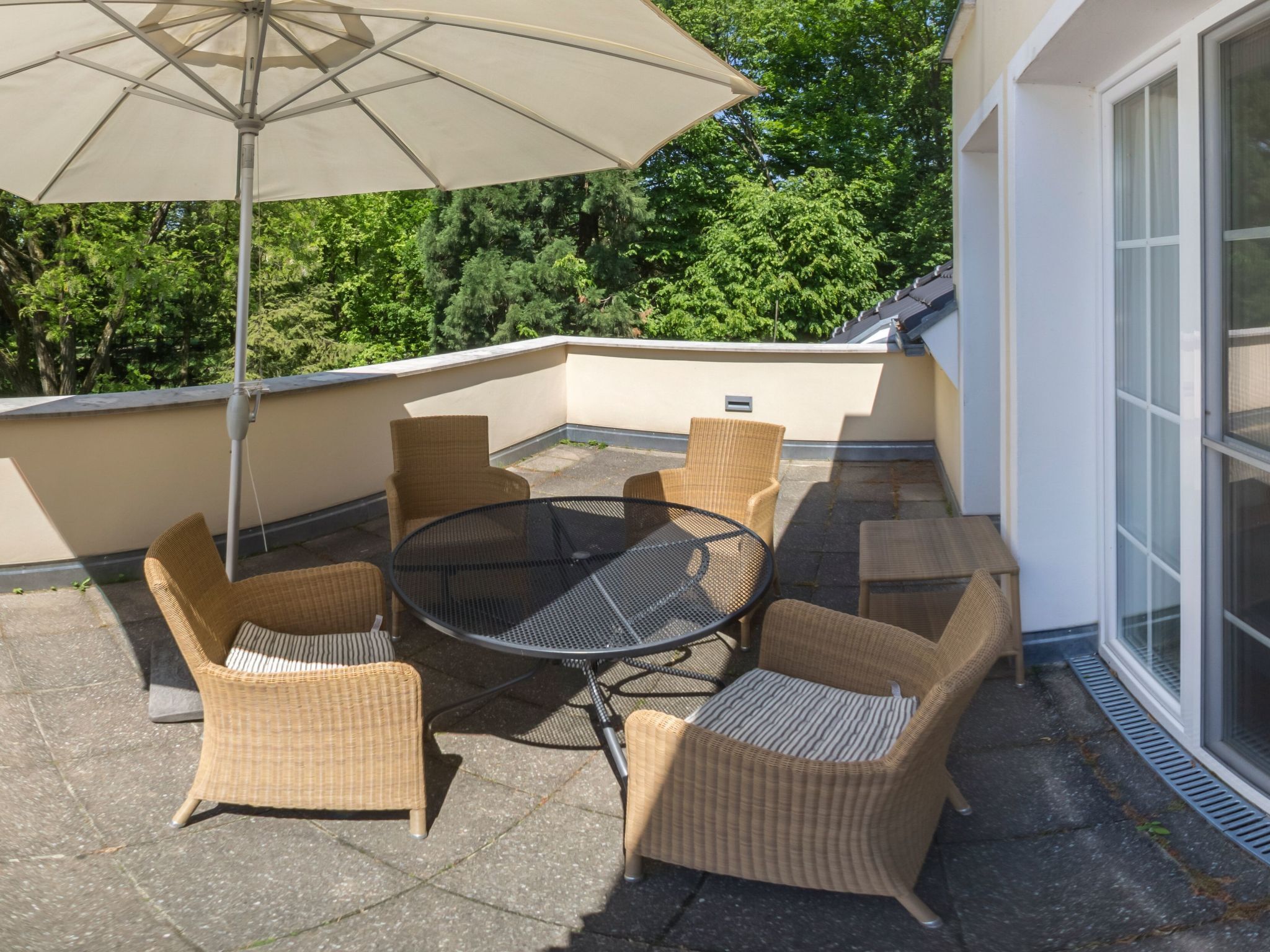 Une terrasse sur le toit, avec une table ronde et des chaises en osier, entourée d’un grand parasol.