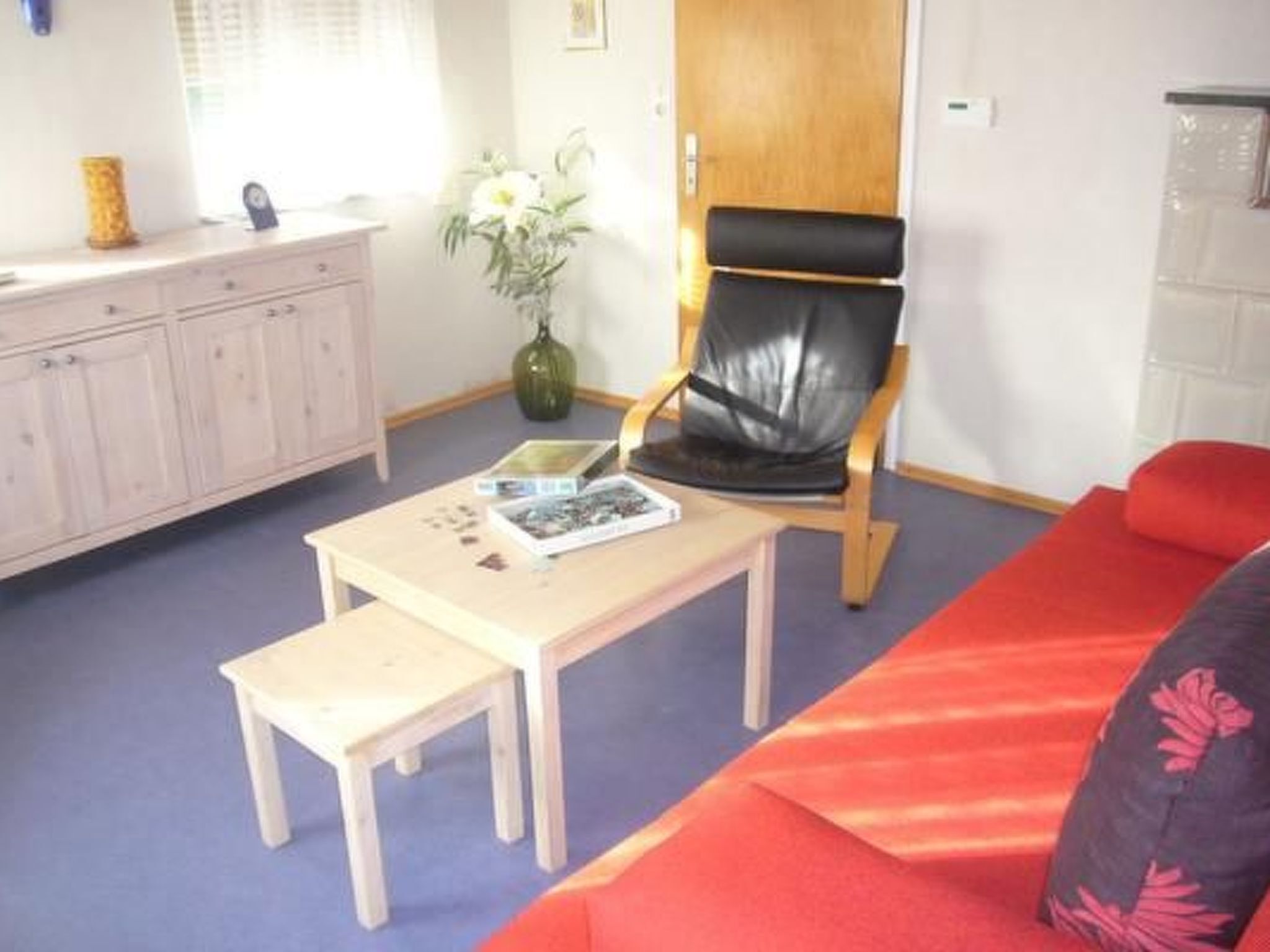 A room with a wooden chair, a small table with a book, a sofa, and a cabinet.