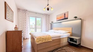 Une chambre à coucher comprenant un lit, une table de chevet, une commode, des rideaux, un tableau, un lustre et une vue sur l’extérieur, visible à travers une porte coulissante.