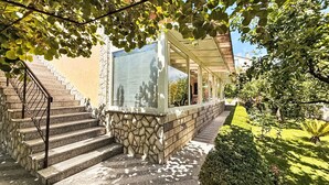 Un escalier en pierre mène à un porche abrité d’où l’on peut admirer un jardin et un bâtiment situé au loin.