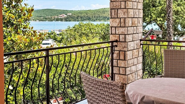 Un balcon agrémenté d’un pilier en pierre, de meubles en osier et offrant une vue sur un lac et des collines.