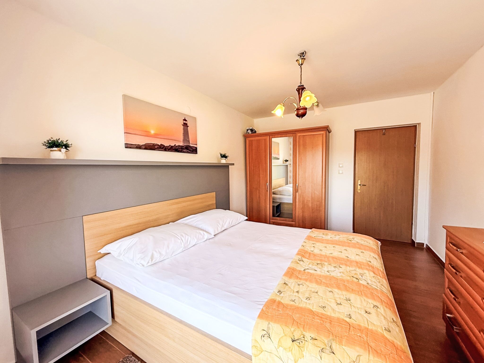Une chambre à coucher comprenant un lit, une table de chevet, une armoire, un miroir et un tableau représentant un phare accroché au mur.
