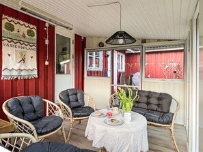 A room with wicker furniture, a table with a white tablecloth, and a red wall with a decorative piece. - Idyllisch gelegenes, ebenerdiges Haus mit Terrasse by Interhome (Svenljunga)