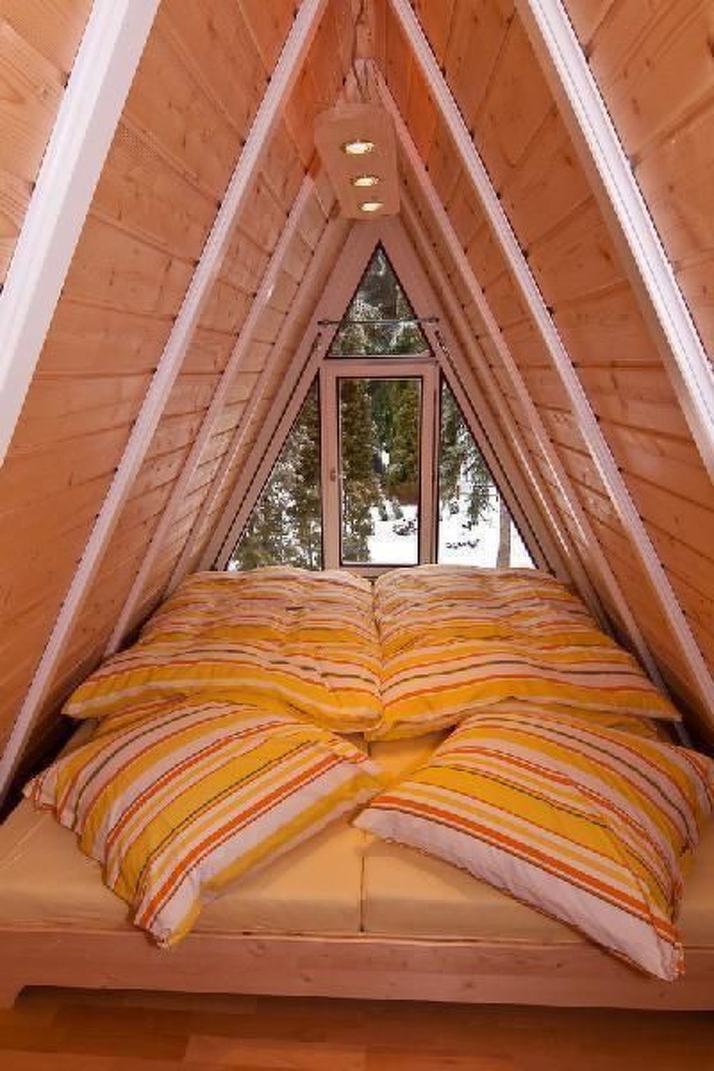 Ein raumförmiger Holzbau mit einem Bett unten, einem Fenster oben und einer Leuchte darüber.