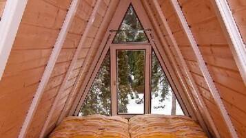 Ein raumförmiger Holzbau mit einem Bett unten, einem Fenster oben und einer Leuchte darüber.
