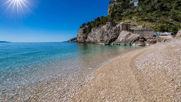 A pebble beach with clear water, a rocky cliff, and a building on top. - Vacation home Stepča by Interhome (Brseč)