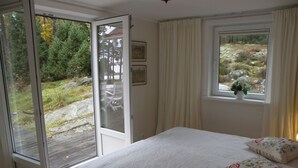 Une chambre avec un lit, une fenêtre avec des rideaux, une porte donnant sur un espace extérieur et une petite plante posée sur le rebord de la fenêtre.