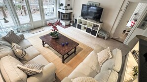 Un salon comprenant un canapé, une table basse, un téléviseur, une cheminée et de grandes fenêtres.