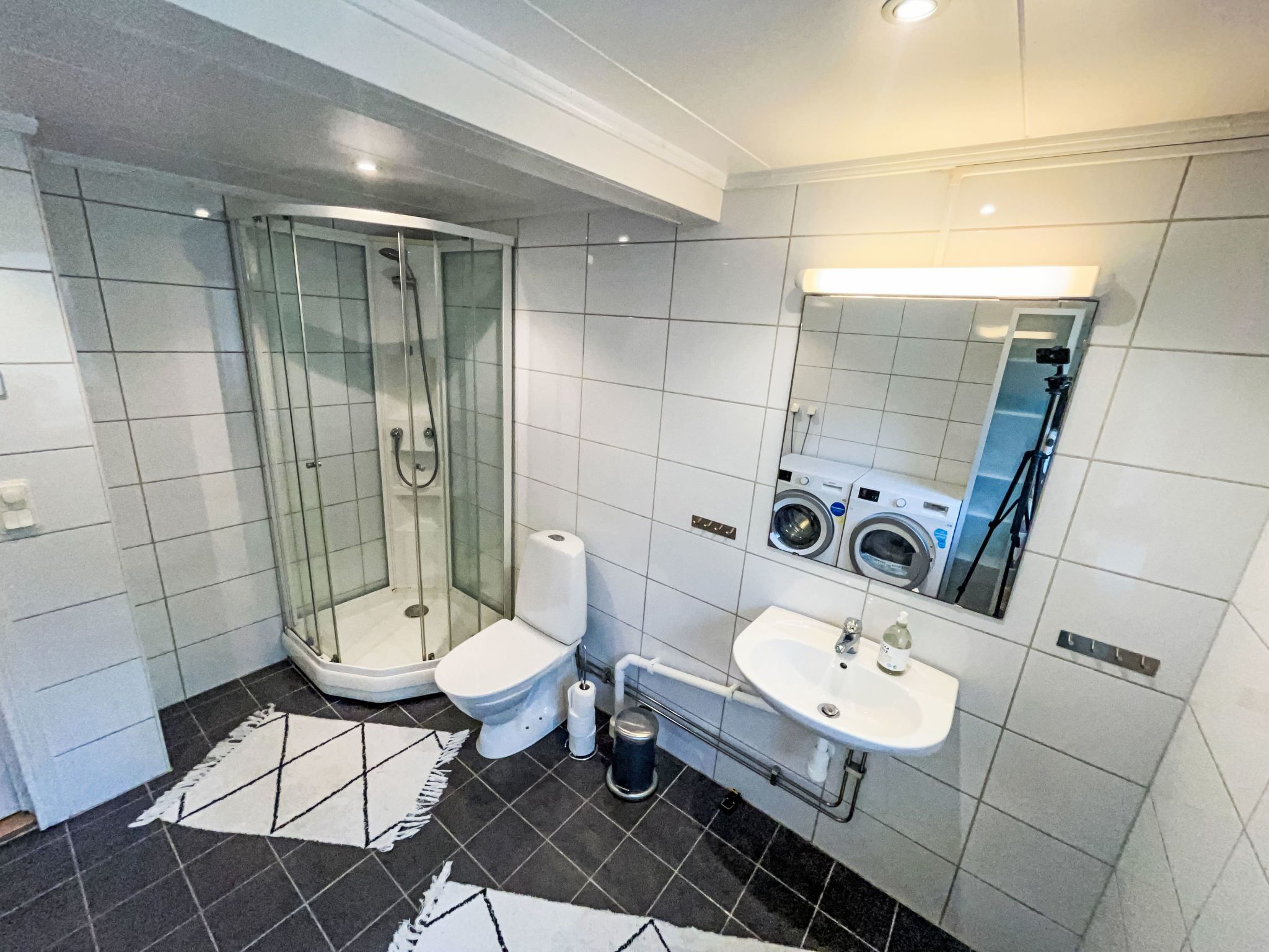 Une salle de bain moderne avec une douche en verre, des toilettes, un lavabo et un miroir qui reflète un lave-linge.