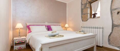 A bedroom with a bed, bedside lamps, a radiator, and a stone wall.