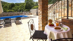 A poolside area with a table set for breakfast, a chair, and a view of the pool and surrounding greenery. - Geräumiges Ferienhaus in Brseč mit Privatem Pool by Interhome (Brseč)