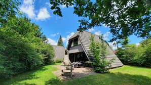 Een rustieke hut met een schuin dak, omringd door weelderige begroeiing en een heldere blauwe lucht.