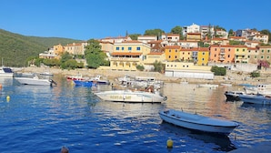 Una pittoresca cittadina costiera con edifici colorati, un porto turistico con diverse imbarcazioni e un cielo azzurro limpido.