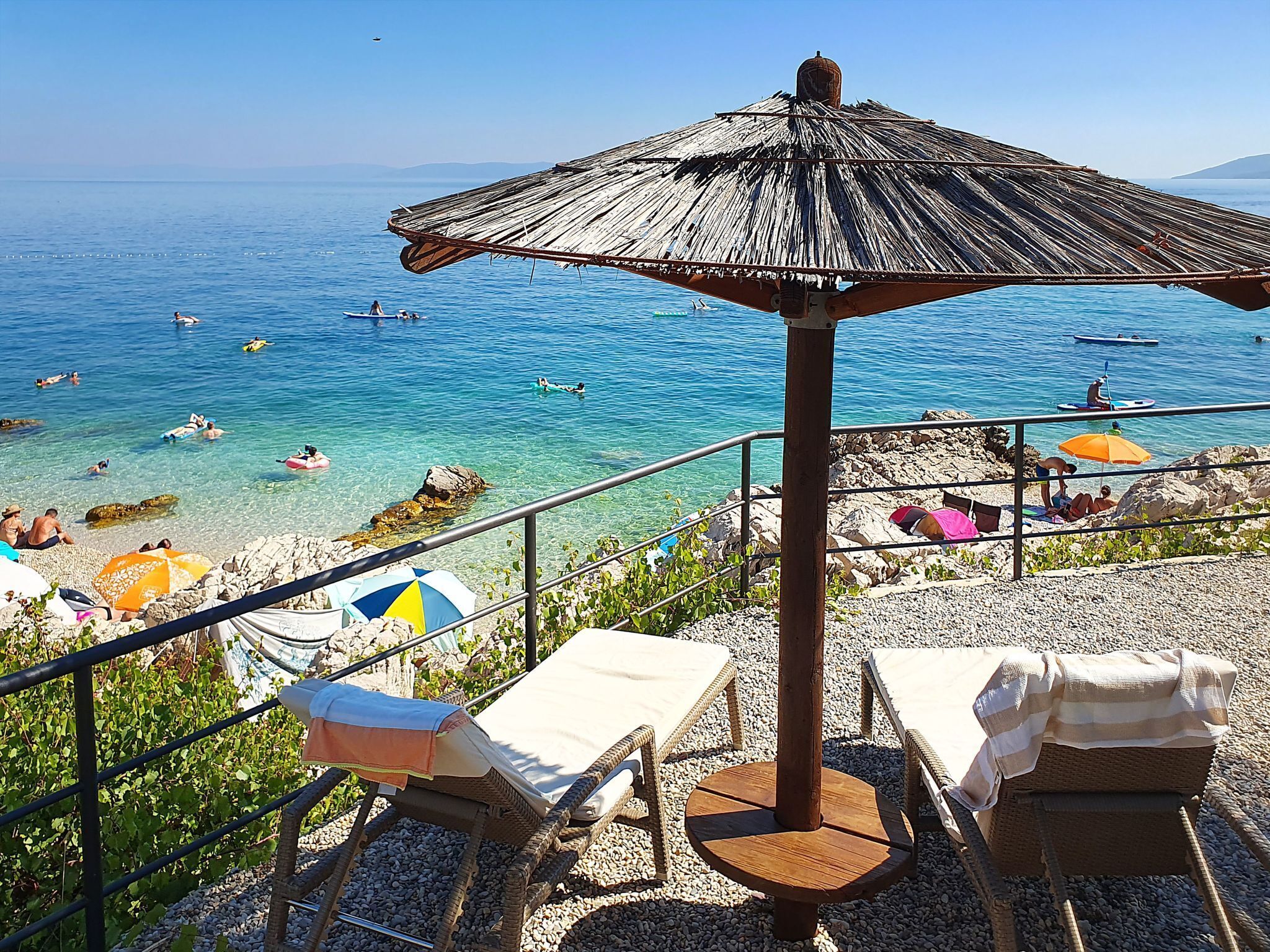 A beachside view with clear blue waters, lounge chairs, and umbrellas.