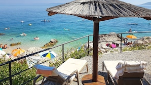 Vista sulla spiaggia con acque cristalline, sedie a sdraio e ombrelloni.