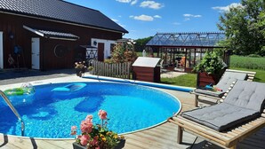 Quintal com piscina, deck de madeira, cadeiras de descanso e estufa.