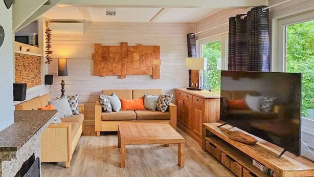 Una sala de estar acogedora con un sofá de madera, una mesa de centro y un televisor. Hay una chimenea, una ventana con cortinas y una pared de piedra.