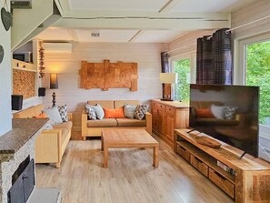 Una sala de estar acogedora con un sofá de madera, una mesa de centro y un televisor. Hay una chimenea, una ventana con cortinas y una pared de piedra.