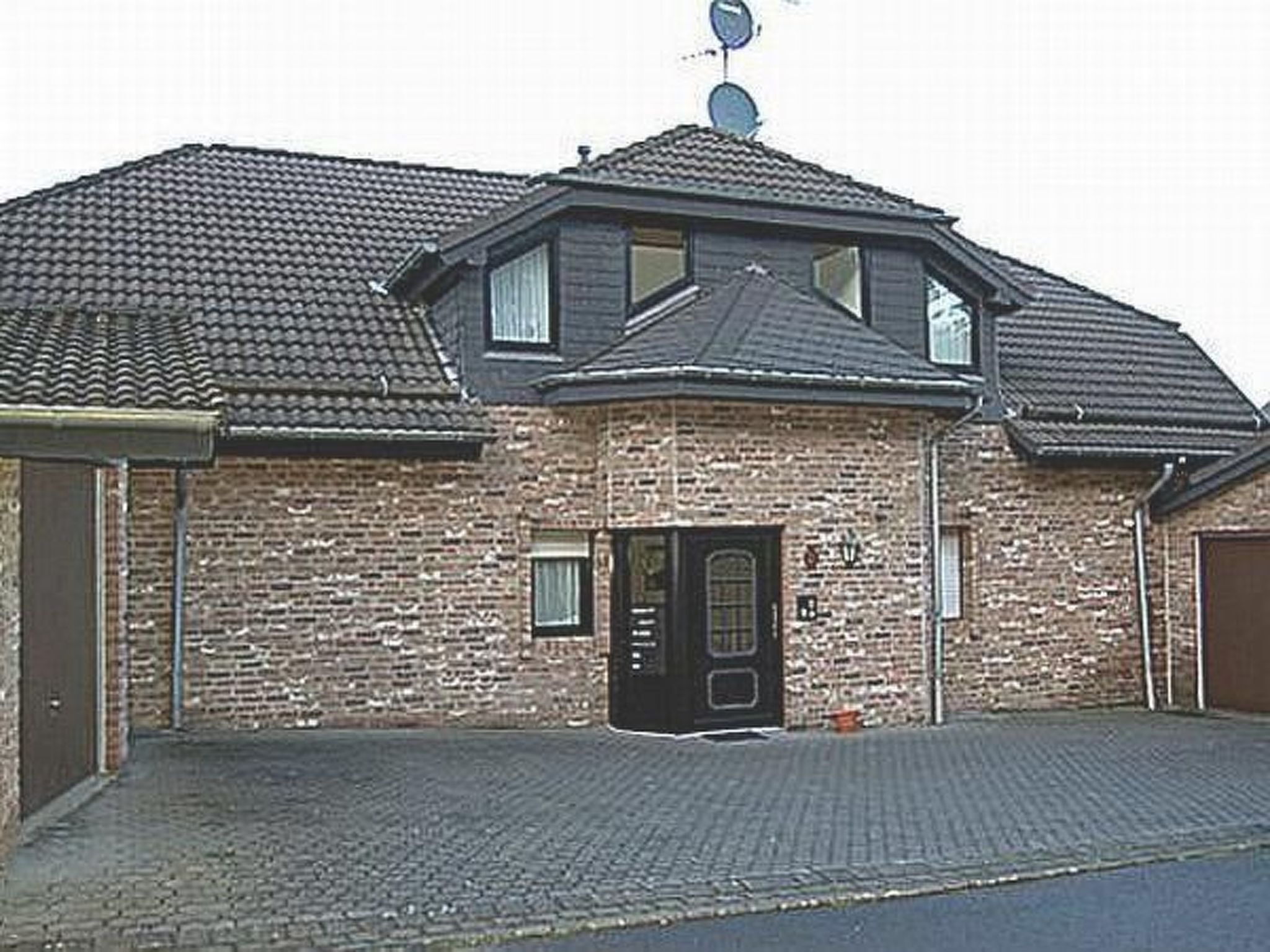 Ein zweistöckiges Backsteinhhaus mit dunklem Dach, einer Haustür und einer Satellitenschüssel.