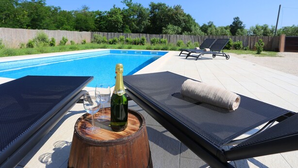 Ein Poolbereich mit Liegestühlen, einer Champagnerflasche und einem Holzbottich.