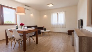 Ein modernes Wohnzimmer mit Essbereich, einer Couch, einem Fernseher und einem Fenster mit Vorhängen.