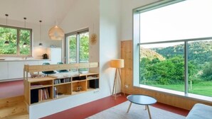 A modern interior with a kitchen, dining area, and large windows offering a view of greenery. - Moderner Holzhausneubau in der Eifel by Interhome (Berlingen)