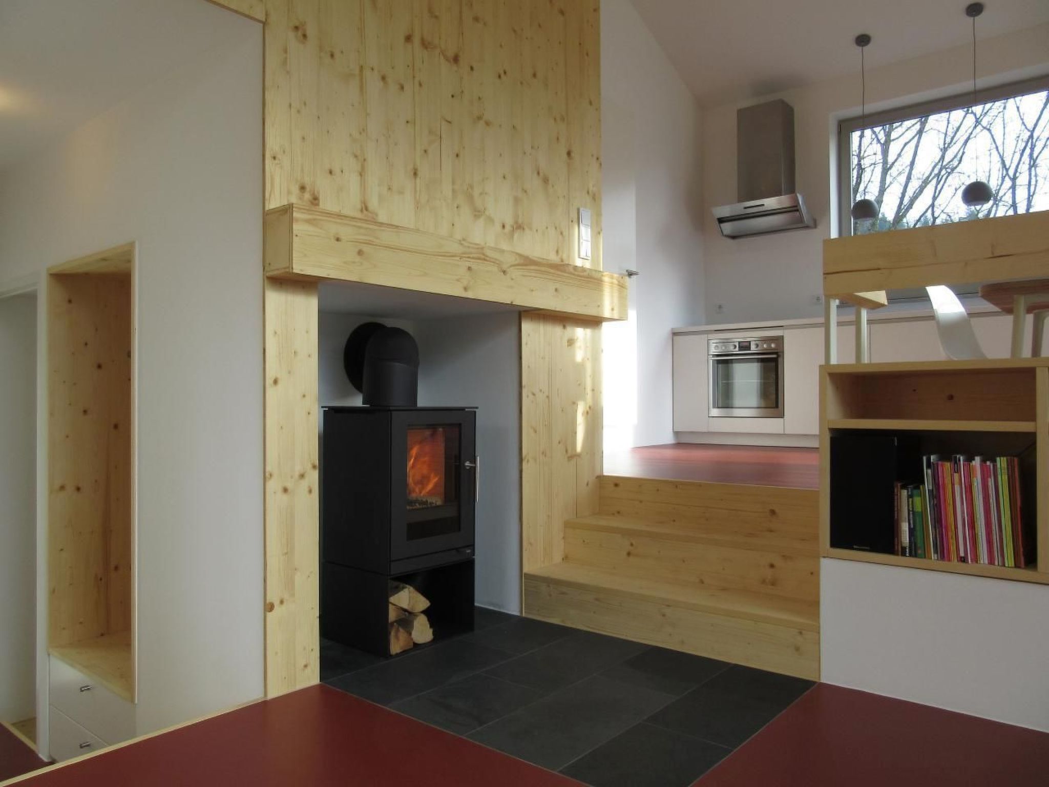 A modern kitchen with a built-in stove, a small oven, and a wooden bookshelf.