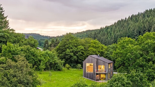 A modern wooden cabin surrounded by lush greenery and a forested hillside. - Moderner Holzhausneubau in der Eifel by Interhome (Berlingen)