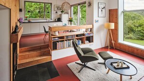 A modern interior with a wooden staircase, a bookshelf, a desk, and a large window offering a view of greenery. - Moderner Holzhausneubau in der Eifel by Interhome (Berlingen)