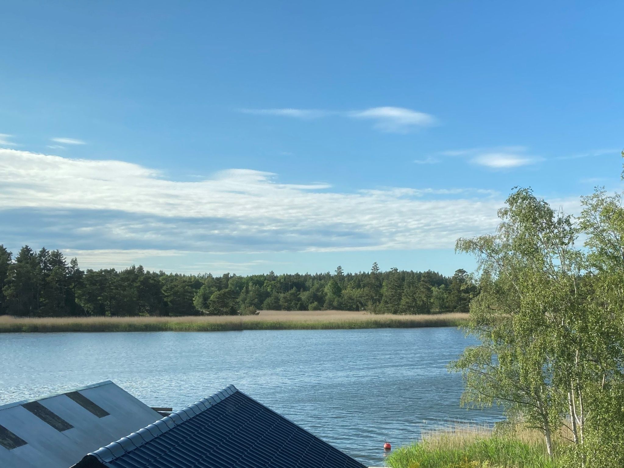 Blick auf ein Seeufer mit einem Gebäude mit geneigtem Dach und einem roten Bojen.