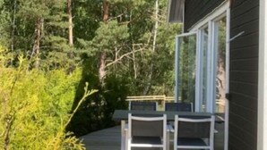 Une terrasse en bois avec deux chaises et une table, entourée de verdure et d’arbres.