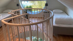 Une pièce dotée d’une lucarne circulaire, d’un lit blanc et d’une balustrade blanche.