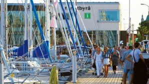 Un port de plaisance avec des bateaux amarrés, un bâtiment avec une enseigne et des personnes se promenant sur le quai.