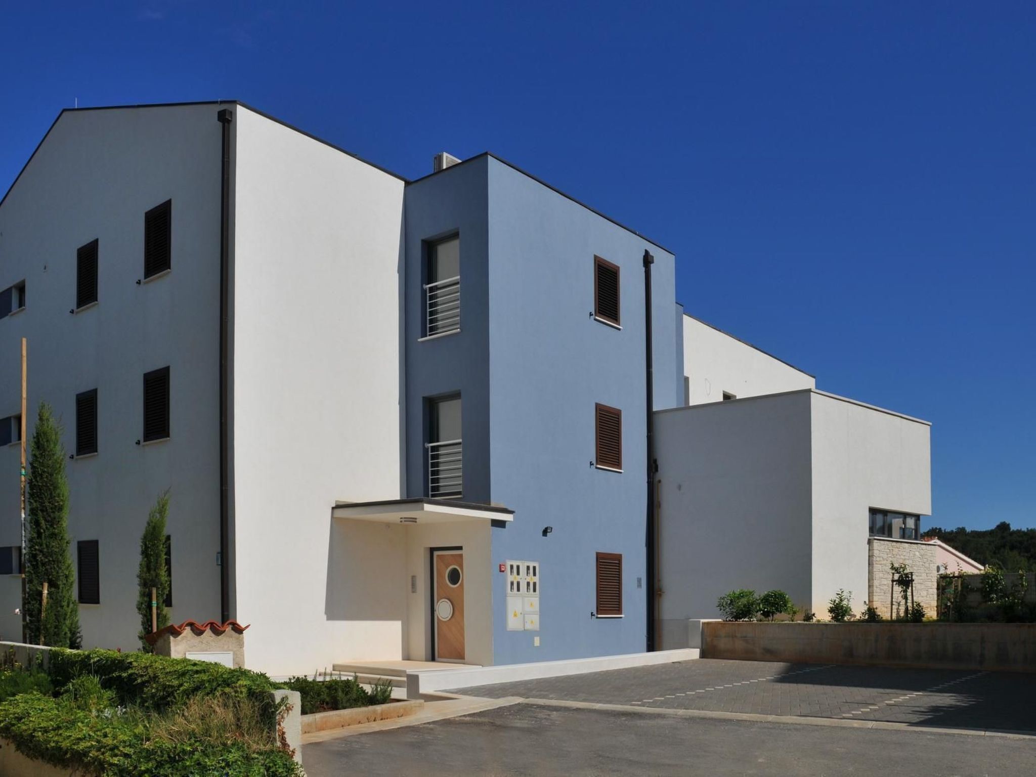 A modern two-story building with a flat roof, a central entrance with a door, and a small porch area.
