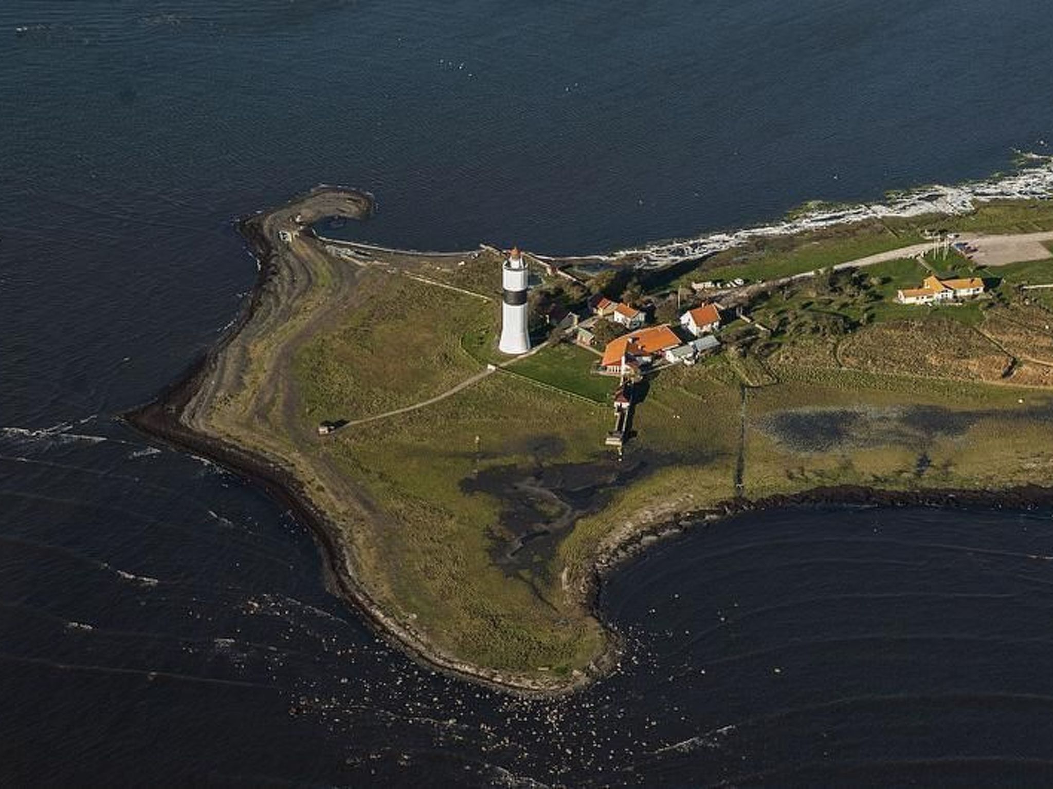 Oversigtsbillede af et kystområde med et fyrtårn, en lille bebyggelse med huse og en bugtet kystlinje.