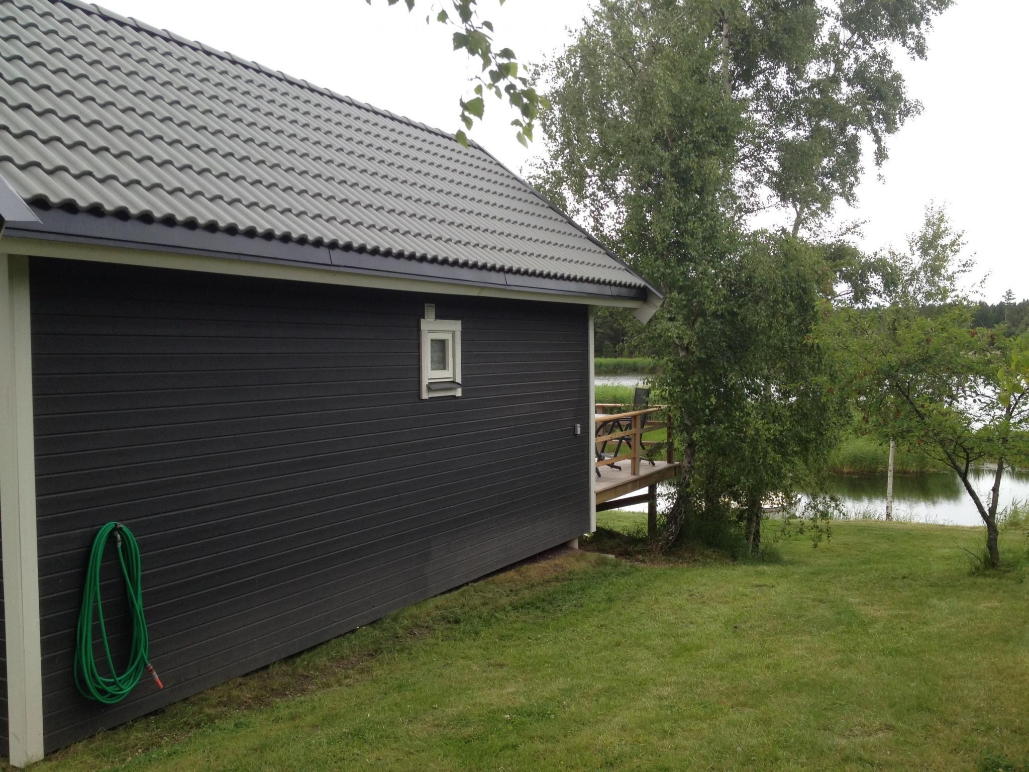 Een donker gebouw met een pannendak, een klein raam en een groene tuinslang aan de zijkant.
