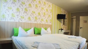 Habitación de hotel con una cama grande, almohadas verdes y blancas, un televisor de pantalla plana montado en la pared y una mesita de noche con teléfono.