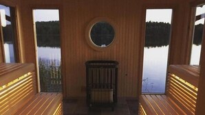 Ein Saunaraum mit Bänken und einer Mittelbank, großen Fenstern mit Seeblick und einem runden Spiegel an der Wand.