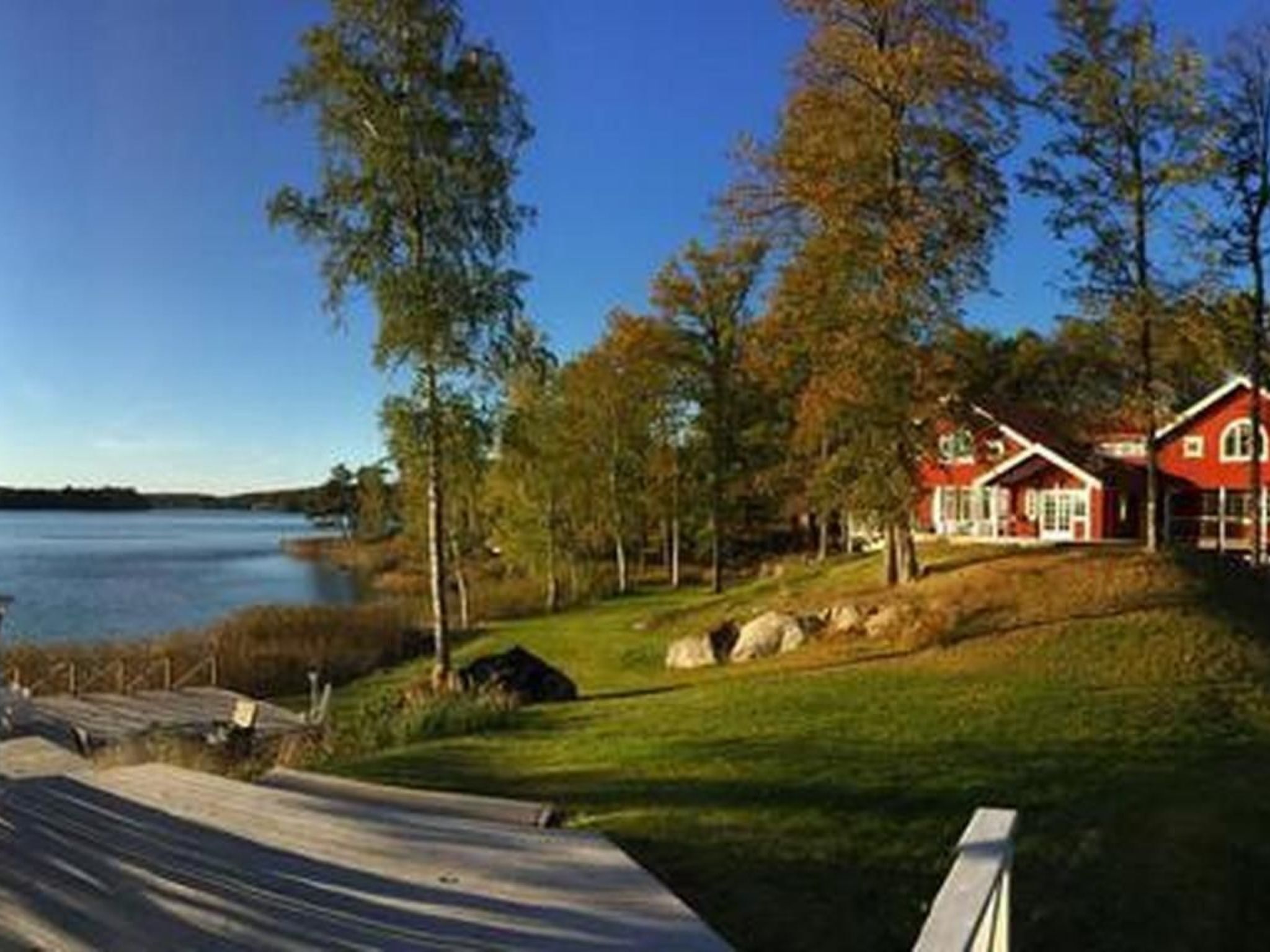 A lakeside property with a wooden deck, red cabins, and a clear view of the lake.