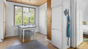A compact room with a wooden ceiling, a dining table with chairs, a white wardrobe, and a view of greenery through the window. - Rosenhill by Interhome (Pauliström)