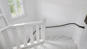 A white staircase with a handrail, a window with a view of greenery, and a white wall. - Rosenhill by Interhome (Pauliström)