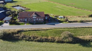 Ein Landhaus mit rotem Dach, umgeben von grünen Feldern und einer Straße.