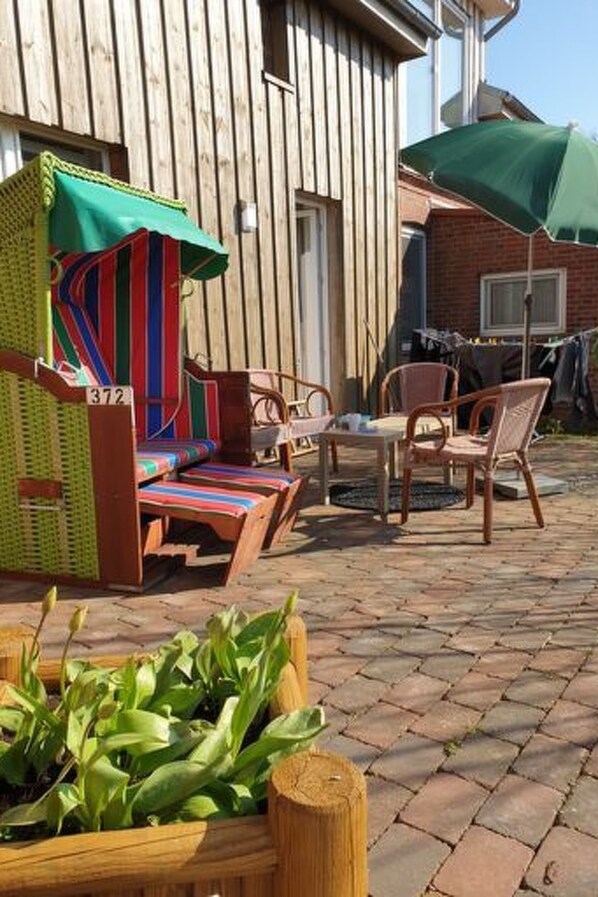 An outdoor seating area with wicker furniture, a wooden table, and a green umbrella. - Wiesenblick by Interhome (Pellworm (Ort))