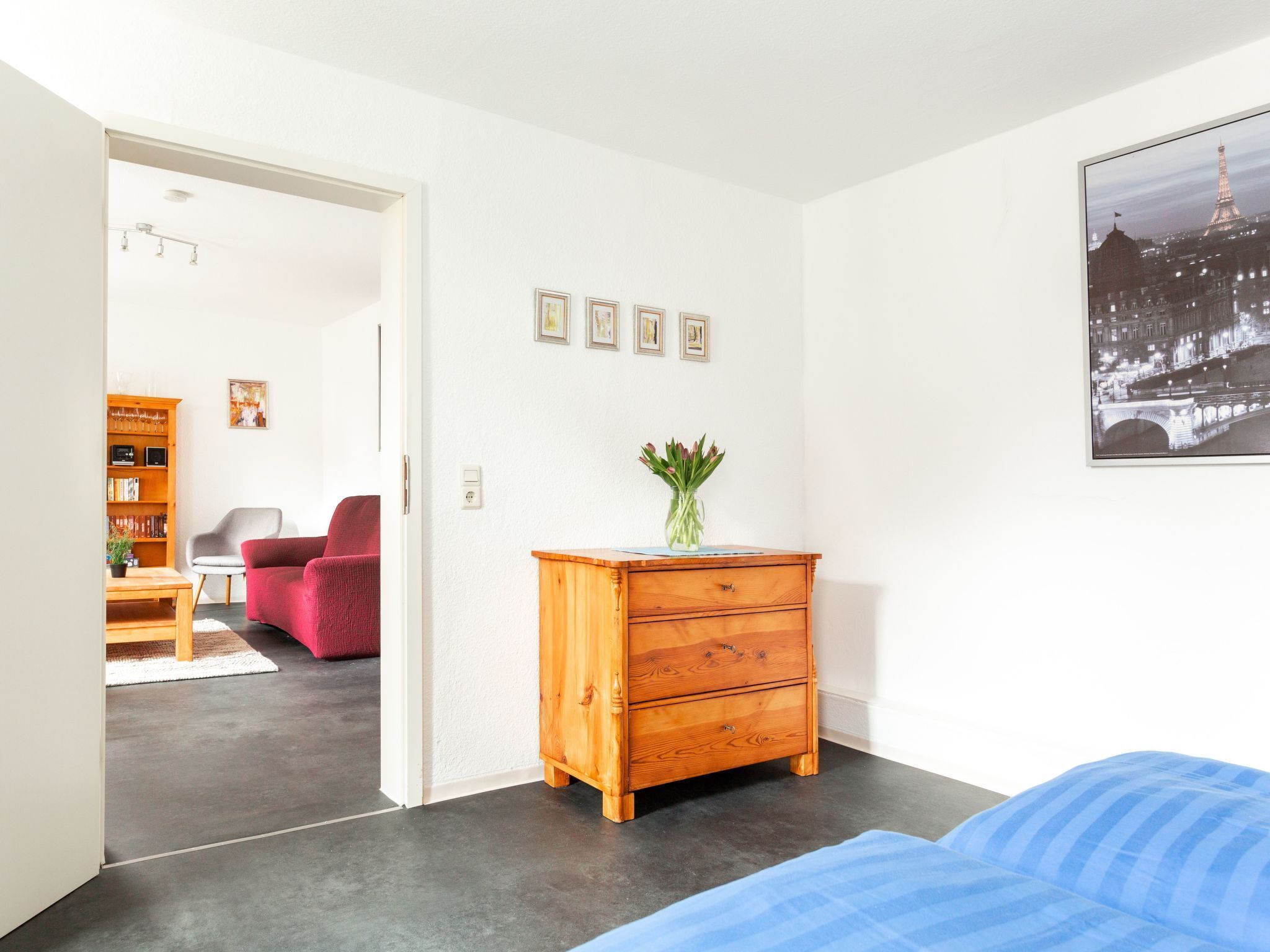 A modern bedroom with a bed, a wooden dresser, a chair, and a bookshelf.