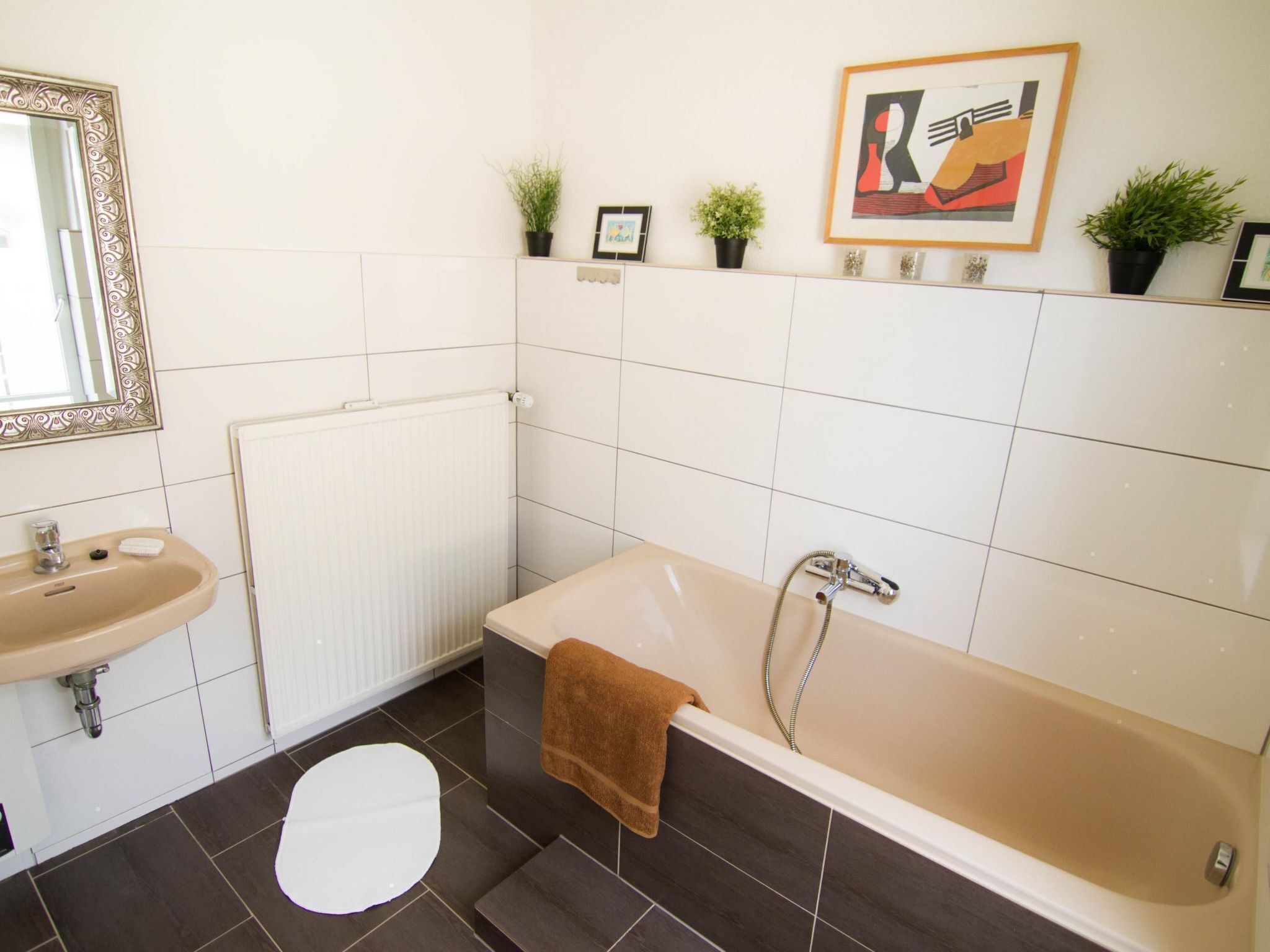 A bathroom with a bathtub, a sink, a mirror, and a radiator. There are potted plants on the wall and a towel on the tub.