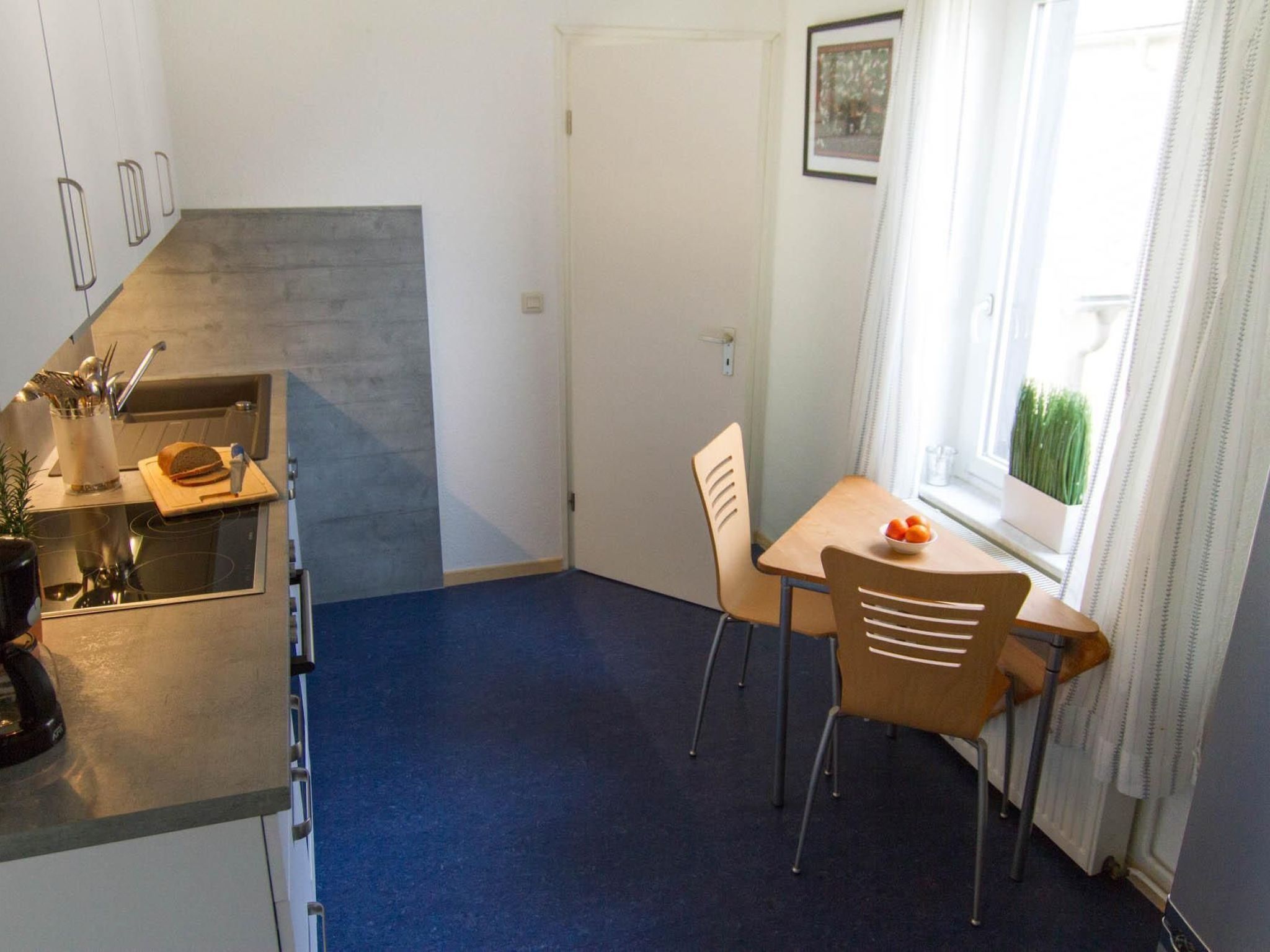 A compact kitchen with a built-in stove, a small dining table with two chairs, and a window with curtains.