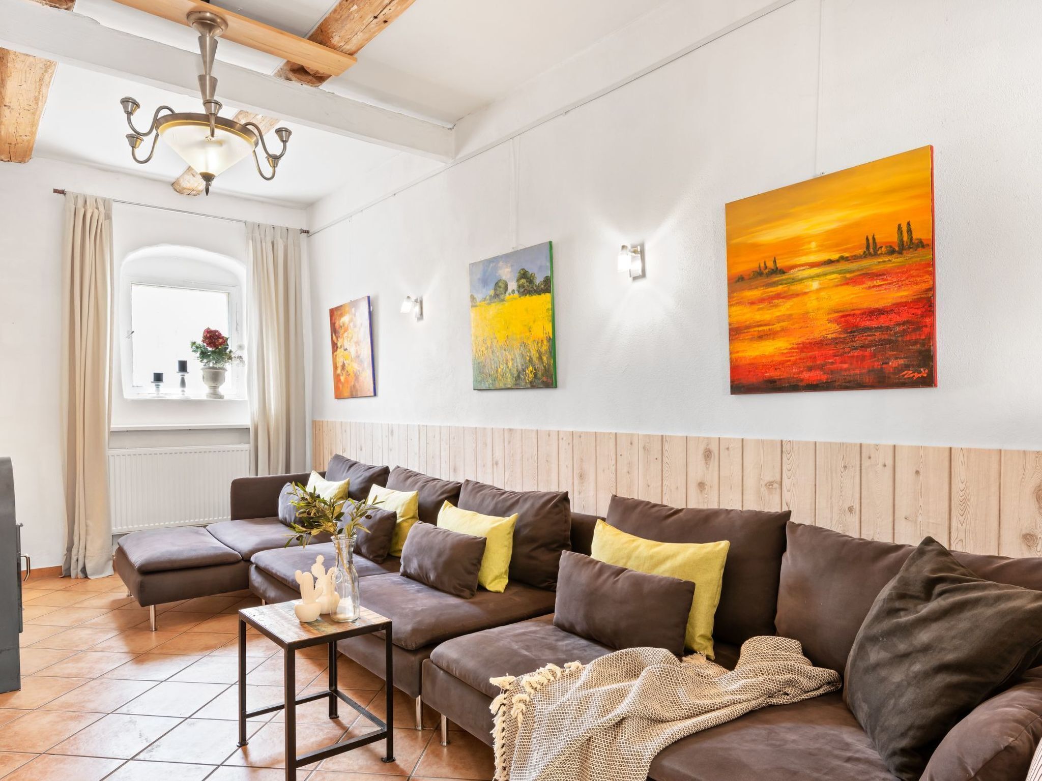A modern living room with a sectional sofa, a wooden accent wall, and a large painting of a sunset.