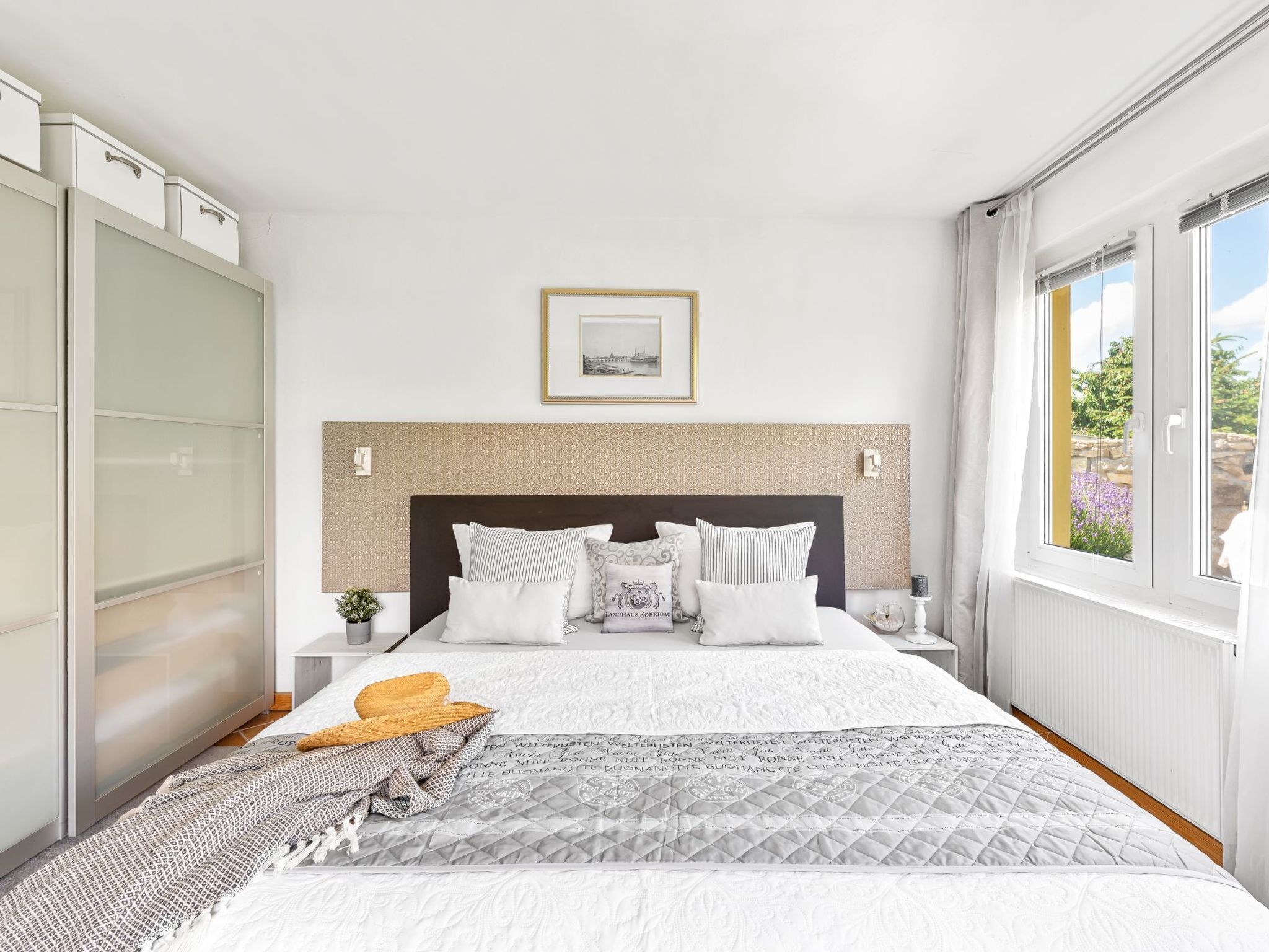 A bedroom with a bed, a headboard, a bedside table, a nightstand, a window, and a view of the outdoors.