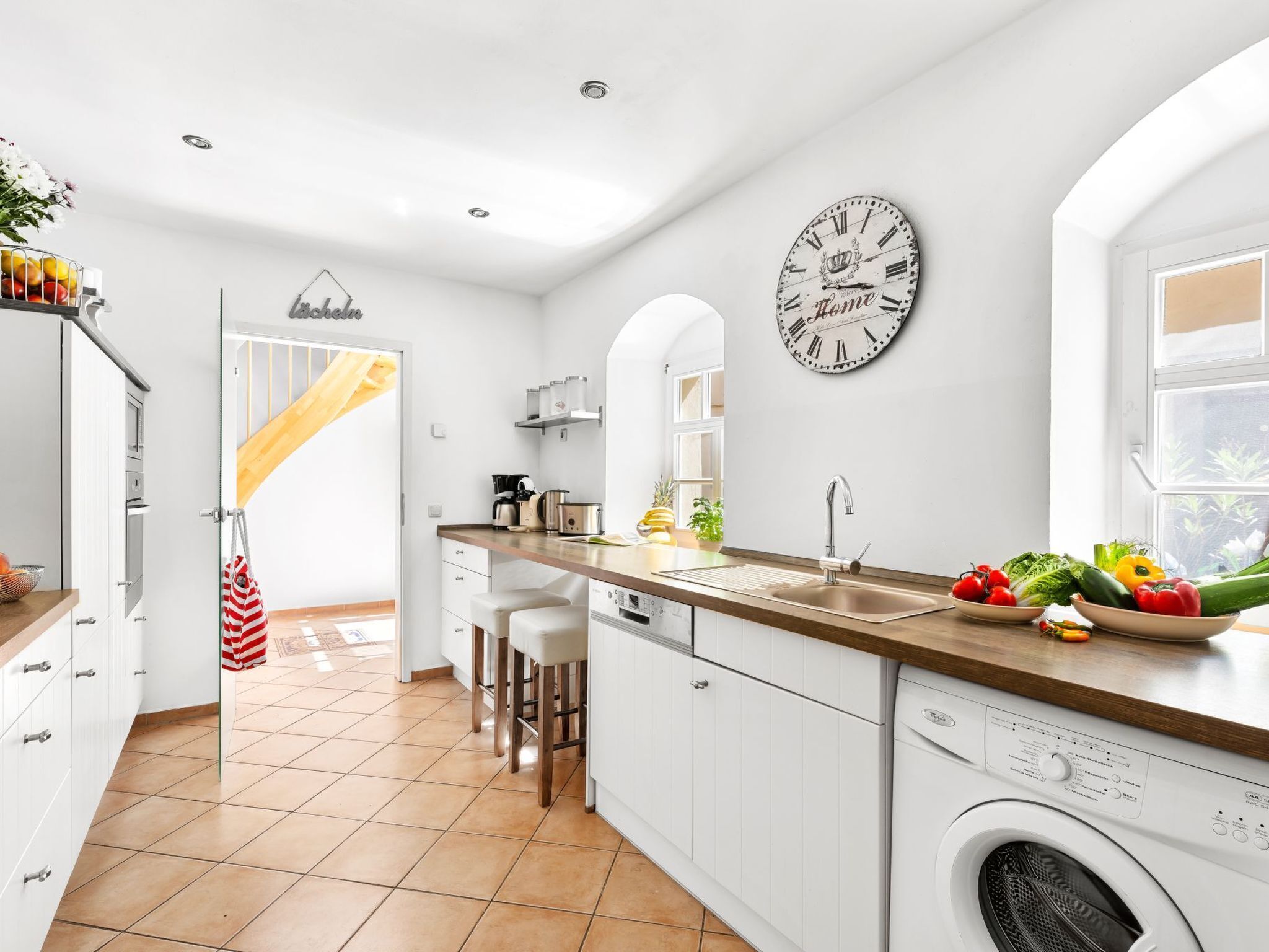 Una cocina moderna con armarios blancos, encimera de madera, lavadora incorporada y un reloj en la pared.